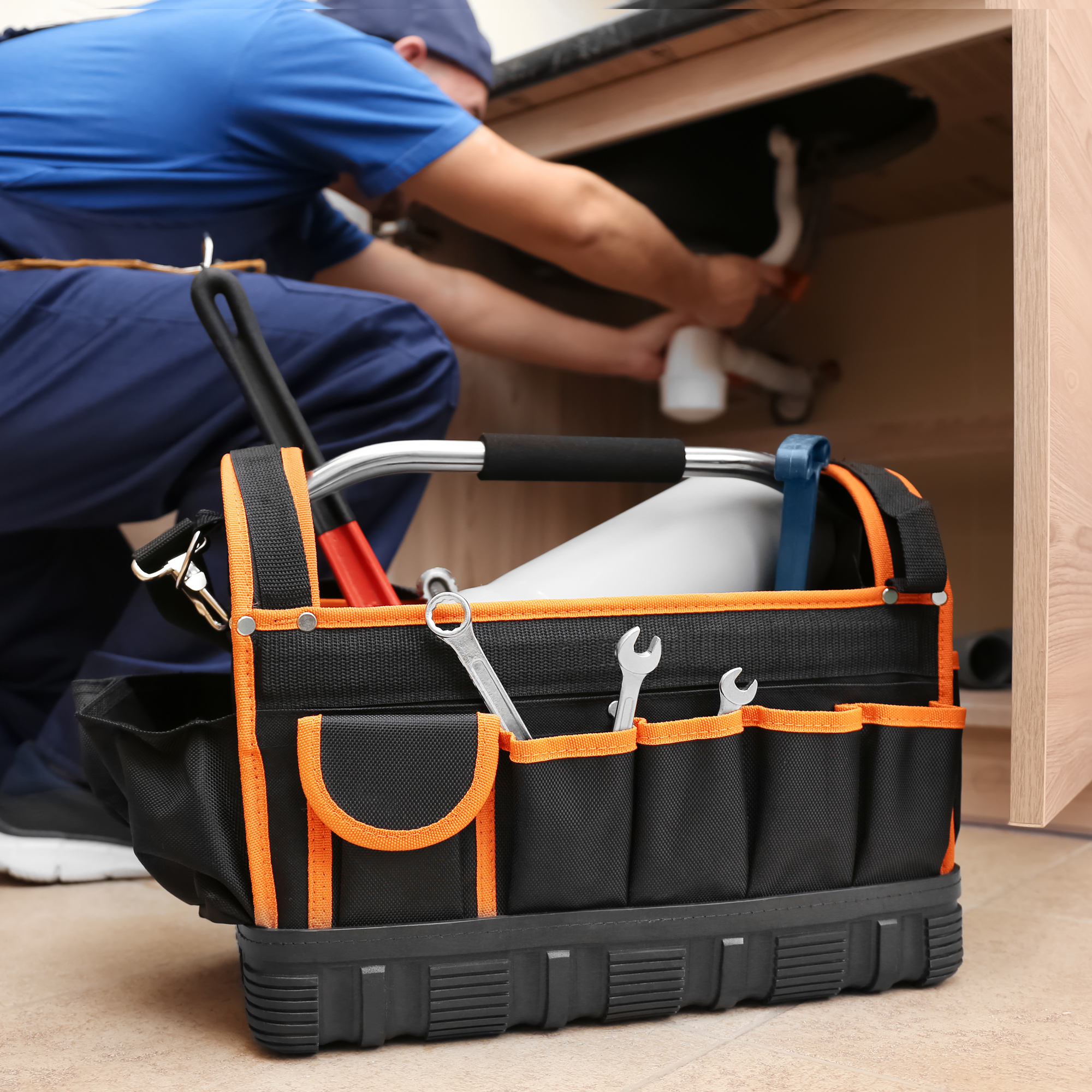 man plumber looking under sink at pipes with tool bag